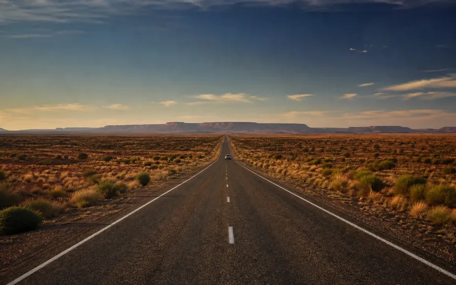 Remote Australian highway crossing red desert plains toward distant mesas